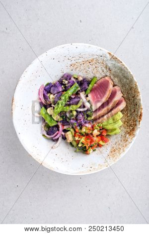 Modern fried tuna fish sashimi filet salad with green asparagus blue potatoes und vegetable chili relish as top view on a plate with copy space 