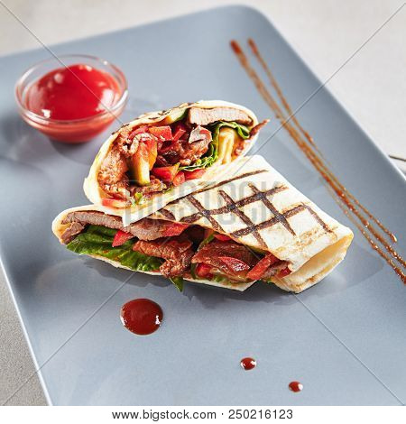 Barbeque Meat Shaverma or Doner Kebab with Vegetables on Blue Plate. Thin Tortilla Rolls Stuffed with Sliced Fried Beef, Pork and Chicken Fillet Cucumber, Tomato, Sauce, Paprika and Greens