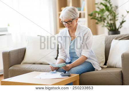 finances, savings, annuity insurance and people concept - senior woman with calculator and bills counting money at home