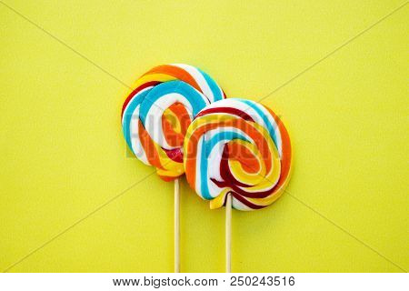 Colorful Hard Candy Lollipop On Yellow Pastel Background. Rainbow Sweet Pattern On Stick Flying Arou