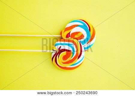 Colorful Hard Candy Lollipop On Yellow Pastel Background. Rainbow Sweet Pattern On Stick Flying Arou