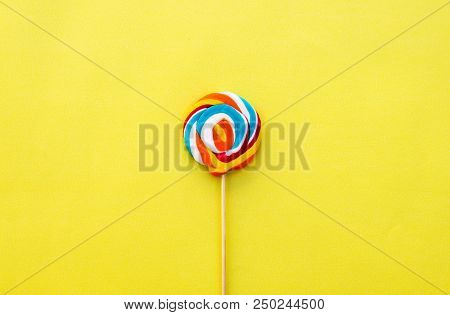 Colorful Hard Candy Lollipop On Yellow Pastel Background. Rainbow Sweet Pattern On Stick Flying Arou