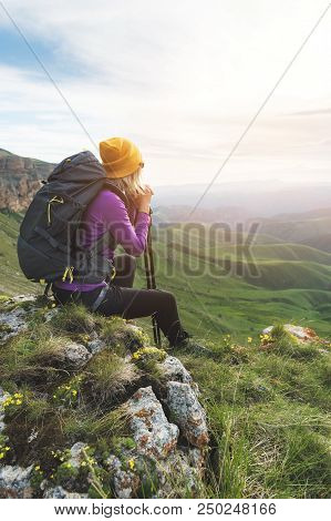 Smiling Girl Traveler In A Yellow Hat And A Pair Of Sunglasses Ssitting At The Foot Of Epic Rocks Wi