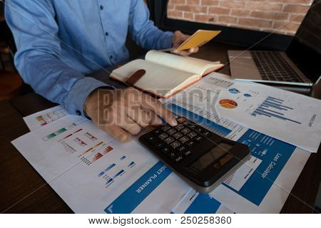 A Man In Blue Shirt Working With Paperwork Calculator And Laptop