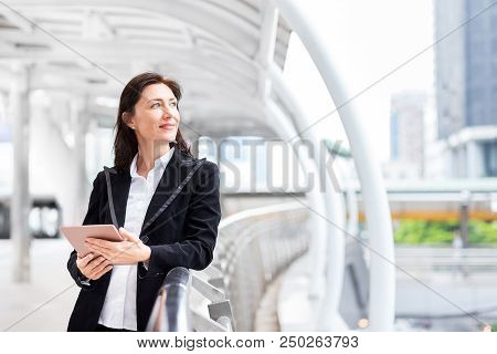 Smiling Business Woman Hold Tablet And Look Out To The Tarket On Walkpath At Downtown Center Of Busi