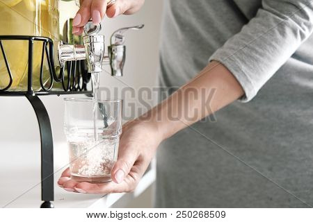 Female Hands Pour Lemonade Out Of The Tap Of The Dispenser. Two Large Glass Jars With Lemon And Lime