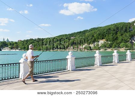 Fisherman With A Fishing Rod Is On The Waterfront Of The Picturesque Lake Abrau In The Caucasus Moun