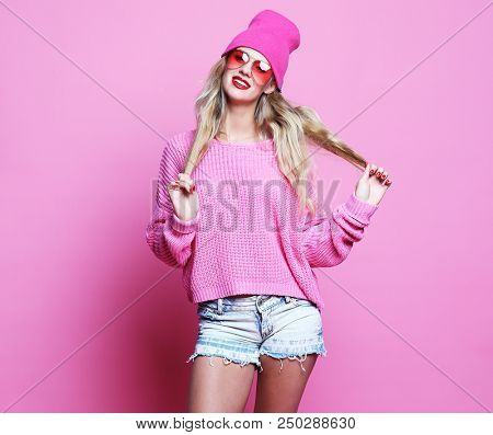 Stylish fashion portrait of trendy casual young woman in pink pulover and hat, posing over pink background. Hipster style.