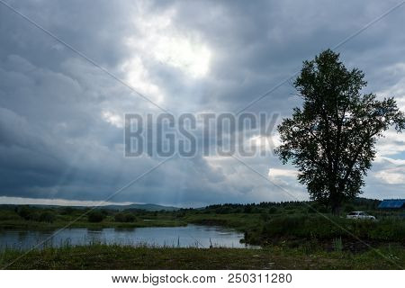 Rural Landscape In Front Of Thunderstorm. Small Lake, Fishermens And Cloudy Sky With Sun Rays. Shot 