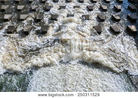 Powerful Flow Of Foaming Water Is Crashing On Small Trapezium Concrete Stones-breakwaters Near The D