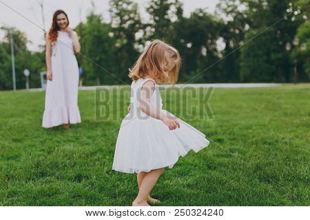 Pretty Little Cute Child Baby Girl In Light Dress Circling Around And Have Fun On Green Grass Lawn I
