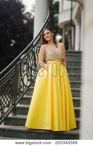 Lady In Yellow Erening Dress Stand On Stairs.