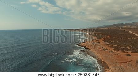 Aerial Photography. The Waves Of The Sea Are Broken Against The Stone Shore. Blue Sky With Fluffy Cl