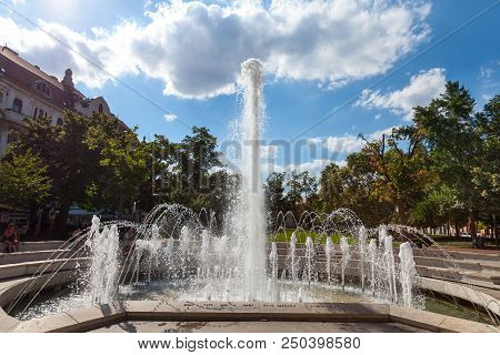 Szeged, Hungary - July 3, 2018: Foutain On Dugonics Ter Square With People Sitting Behind. This Squa