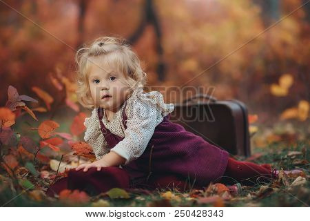 Portrait Of A Cute Little Blonde Girl With Wavy Hair In An Autumn Park