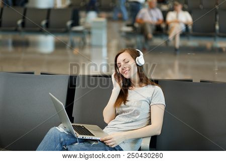 Young Relaxed Traveler Tourist Woman With Headphones Listening Music Working On Laptop, Wait In Lobb