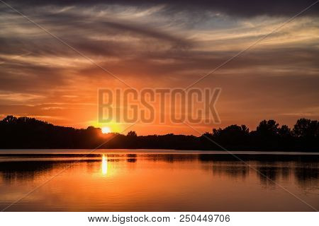 Setting Sun And Sunset Clouds Over Silhouettes Of Trees With Reflection In Water Surface Of Suliansk
