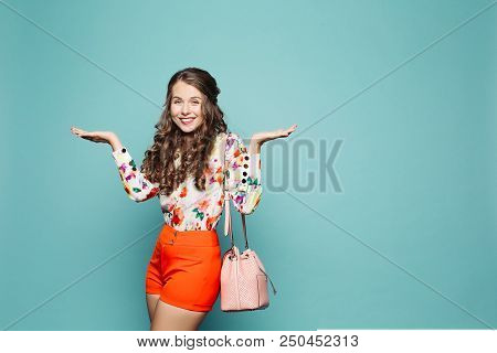 Studio Portrait Of Attractive Woman With Curly Hair Wearing Floral Shirt With Red Shorts And Carryin