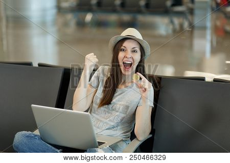 Young Overjoyed Traveler Tourist Woman In Hat Sitting Working On Laptop Holding Bitcoin, Doing Winne