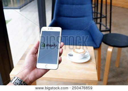 A Man Sit In Cafe Holding Mobile With Shopify Screen