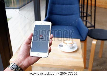 A Man Sit In Cafe Holding Mobile With Udemy Screen