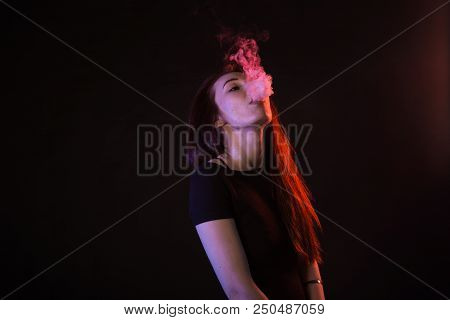 Young Woman In Neon Light And Smoke Of E-cigarettes Or Vape On Black Background.
