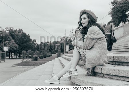 A Beautiful Girl In A Hat, Keeps The Hair From The Wind. Sits On Scraps. Walk Around The City. Portr