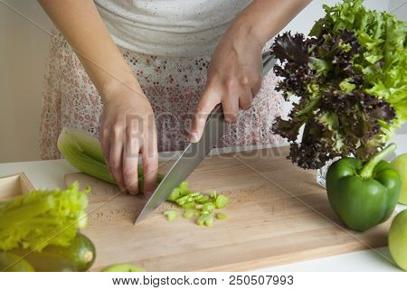 Woman Chopping Celery Vegetable ,preparing Food In Her Kitchen, She Is Cutting Fresh Celery On A Cut