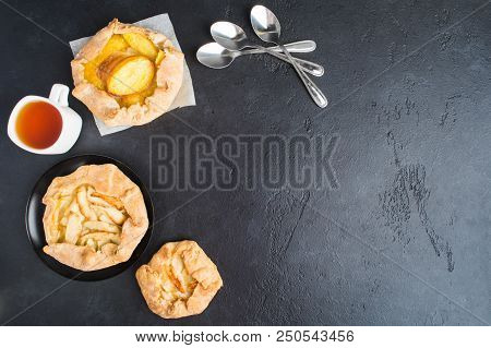 Homemade Sweet Baking With Apples And Appricots With One Cup Of Tea And Spoons Over Black Background
