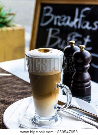 Hot Latte Macchiato Coffee With Tasty Foam And Cinnamon In Tall Clear Glass On Serving Table