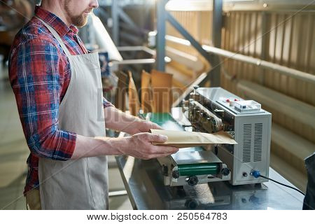 Mid Section Side View Of Man Wearing Apron Packing Freshly Roasted Coffee Beans In Craft Paper Bags 