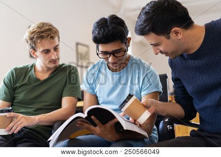 Three Focused Fellow Students Studying Together And Drinking From Disposable Cups. Young Men Sitting
