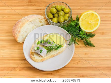Open Sandwich With Slices Of Pickled Herring Fillet On A Saucer And Beside White Bread, Green Olives