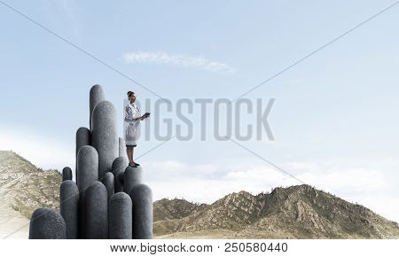 Young Female Doctor With Folder In Hands Satnding On Stone Column