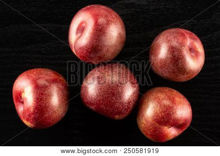 Group Of Five Whole Fresh Pluot Interspecific Plums Variety Flatlay On Black Wood