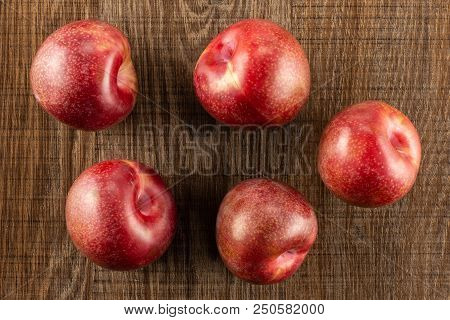 Group Of Five Whole Fresh Pluot Interspecific Plums Variety Flatlay On Brown Wood