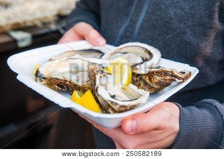 Close Up Male Hand Holding Take Away Food Tray With Fresh Opened Oyster And Lemon Slices At Street F