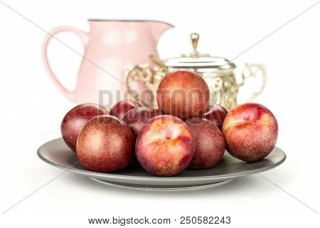 Lot Of Whole Fresh Pluot Interspecific Plums Variety On A Ceramic Grey Plate With A Pink Jar And Sug