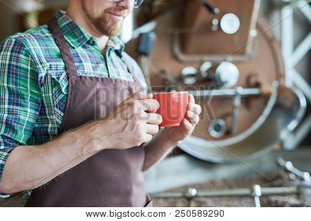 Mid Section Portrait Of Unrecognizable Barista Holding Coffee Cup While Posing Next To Roasting Mach