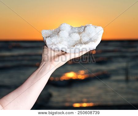 Woman Holding Aurora Rainbow Quartz Cluster From India  In Her Hand At Sunrise In Front Of The Lake.