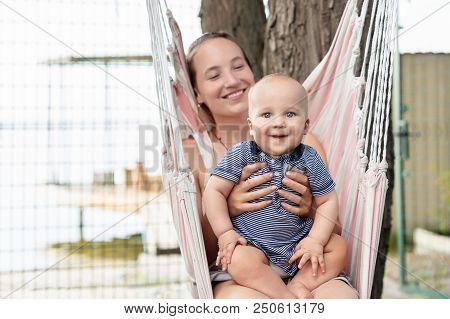 Young Mother With Cute Baby Boy Sitting And Relaxing On Hammock Near River Or Lake. Mom And Kid Havi