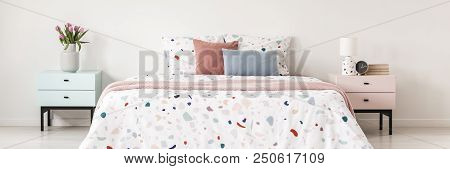 Real Photo Of Two Bedside Tables In Pastel Colors With Fresh Flowers, Clock, Lamp And Books Standing