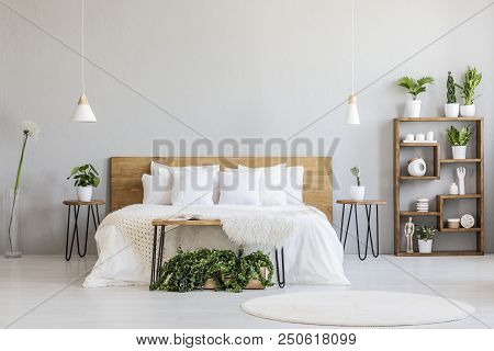 White Pillows On Wooden Bed In Minimal Bedroom Interior With Plants And Round Rug. Real Photo