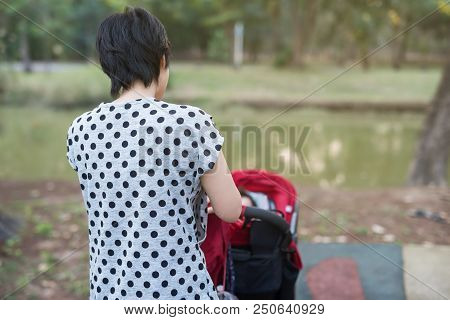 Mother Wheel Red Stroller To Let Her Child Daugther To Relax In Summer Park. Mom Take Care Of Baby G