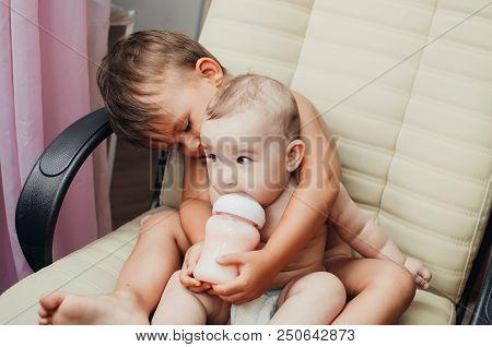 Brother Feeding Little Sister With Milk Or Cereal With A Bottle