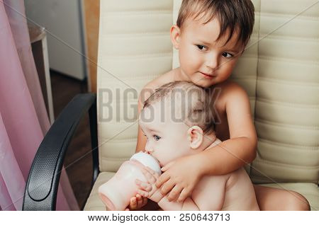 Brother Feeding Little Sister With Milk Or Cereal With A Bottle