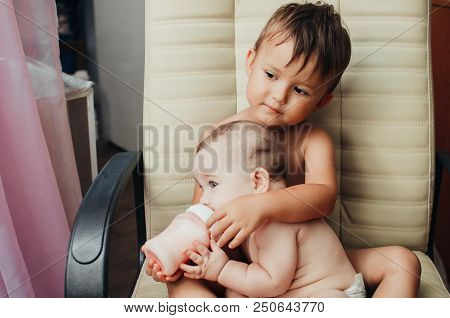 Brother Feeding Little Sister With Milk Or Cereal With A Bottle