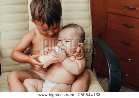 Brother Feeding Little Sister With Milk Or Cereal With A Bottle