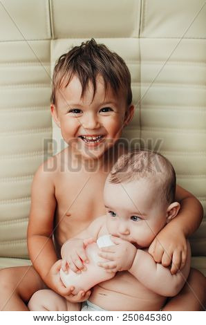 Brother Feeding Little Sister With Milk Or Cereal With A Bottle