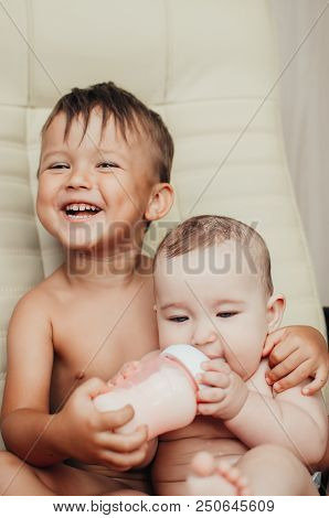 Brother Feeding Little Sister With Milk Or Cereal With A Bottle